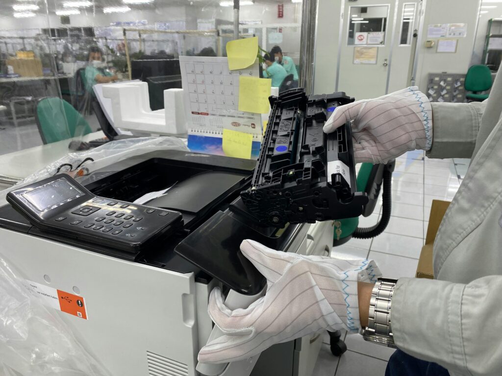A technician wearing white protective gloves carefully removes or installs a toner cartridge into a large office printer within a professional workspace.