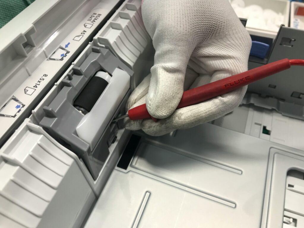 A technician wearing white protective gloves uses a precision tool to perform maintenance or a repair on the internal components of an office printer.