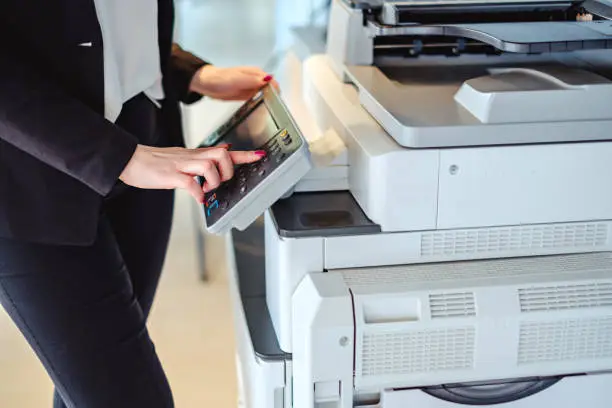 A professional in a business suit operates the control panel of a large office multifunction printer.